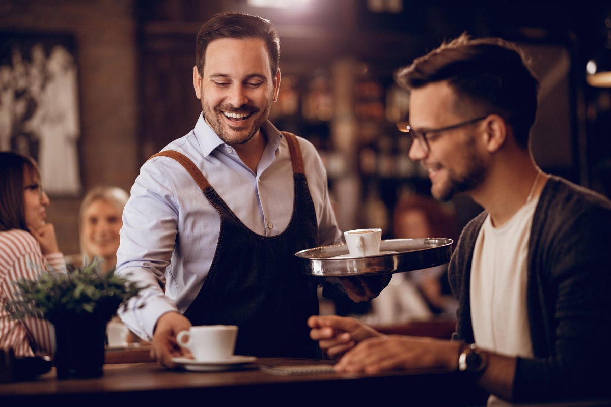 uomo-felice-che-serve-un-ospite-con-un-caffe-mentre-lavora-part-time-come-cameriere-in-un-bar